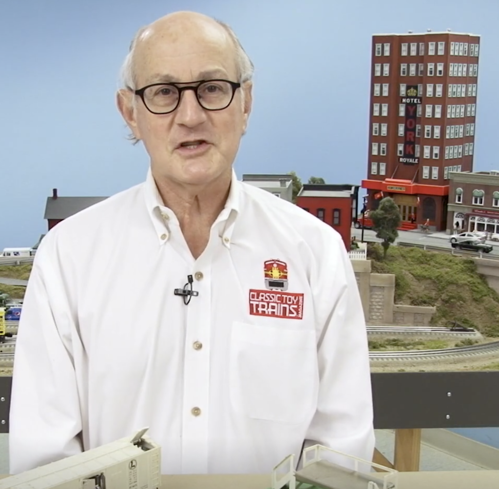 Older caucasian male standing in front of a toy train layout.