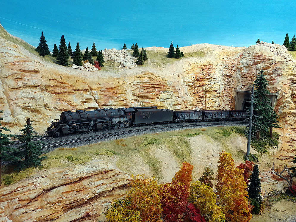 Santa Fe 2-8-8-2 steam locomotive pulls empty hoppers out of tunnel onto mountainous two-track main line