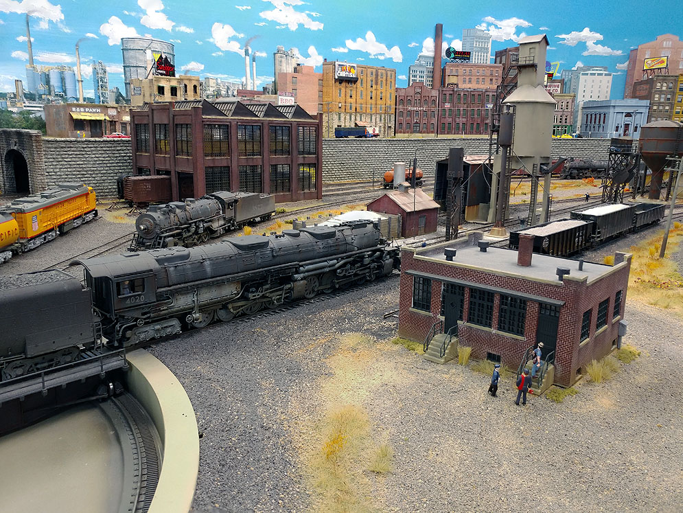 Union Pacific Big Boy moving left to right prepares to leave yard with mixed freight train, dirt rpad in foreground, industrial buildings in background