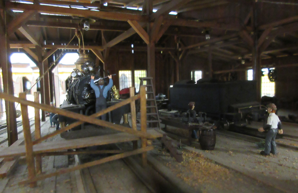 A steam locomotive being worked on is seen through the doorway of a wooden engine shop