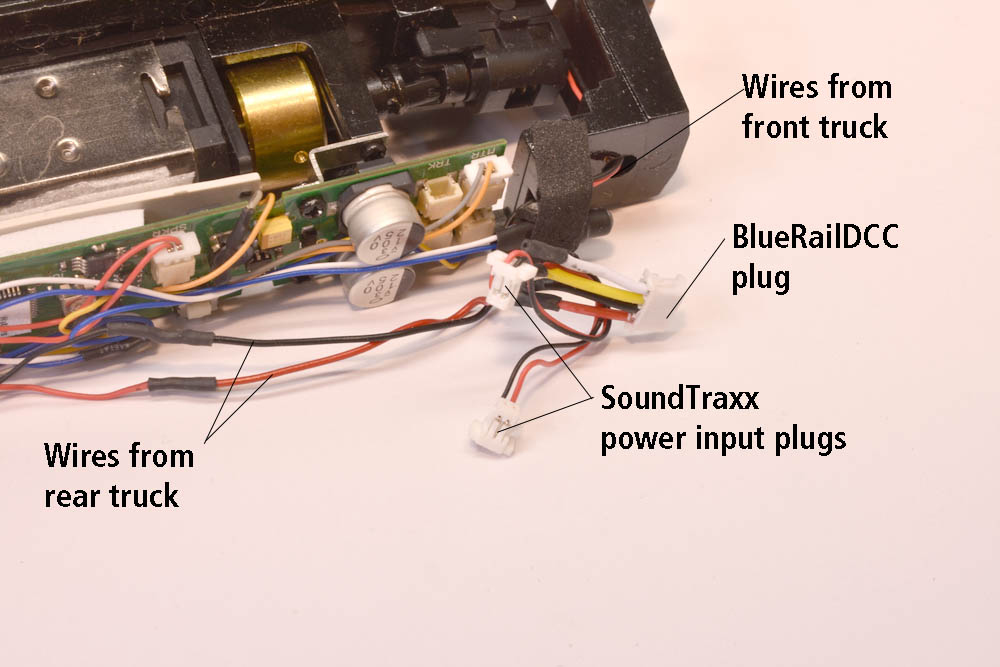 Walthers H10-44 locomotive frame laying on its side with SoundTraxx DCC decoder board, miniature electronic plugs with red and black wires, and larger electronics plug with red, black, yellow, and white wires