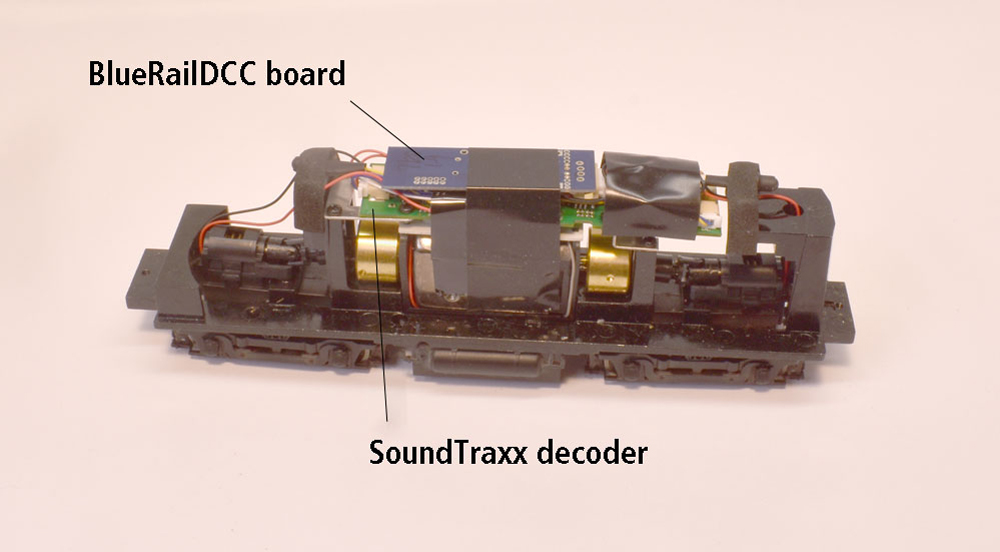 Black die-cast metal frame with can motor, brass flywheels, power trucks, with BlueRailDCC board installed on top of SoundTraxx DCC decoder with strip of black electrical tape