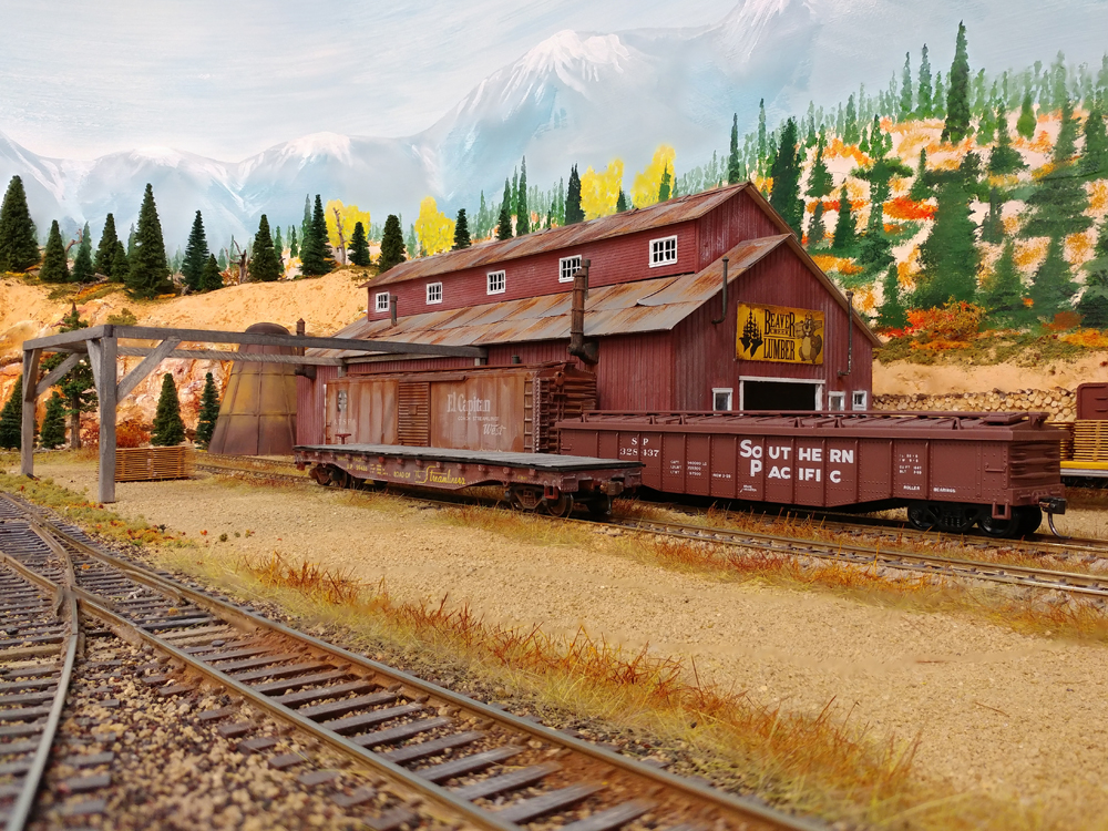 Red board-and-batten building with red Southern Pacific covered gondola, weather beaten red Santa Fe 50-foot boxcar, red flatcar