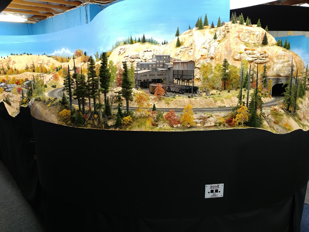 Gray steel coal mine structure in rugged mountain with exposed tan rock faces and tall pine trees