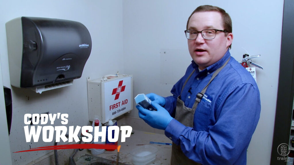 Cody Grivno standing at the sink in the MR workshop holding an unpainted model structure in his hands.