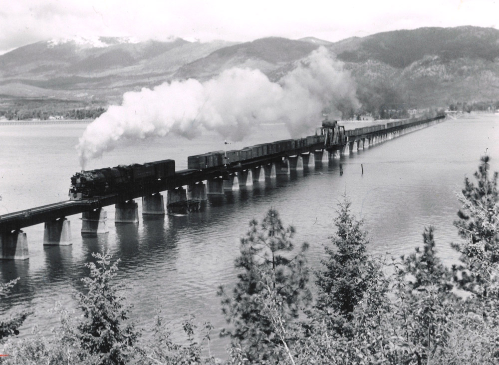Steam locomotive with freight train crossing long, low bridge.