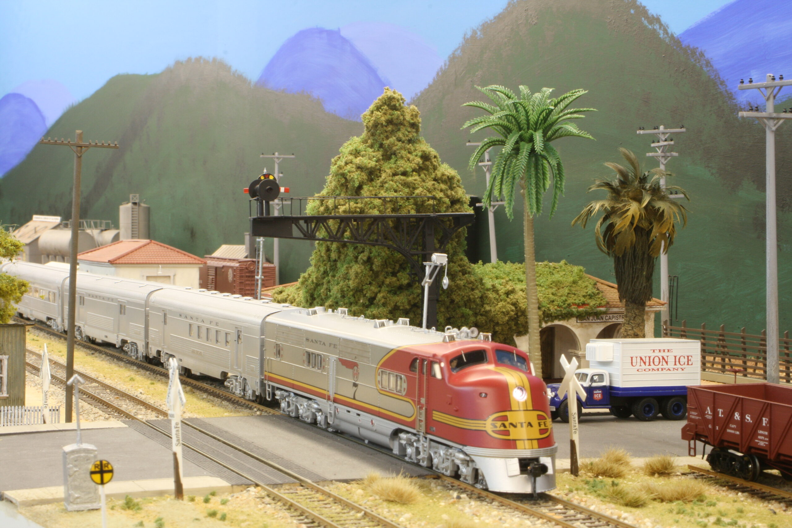 A red-and-silver Santa Fe diesel leads a streamlined passenger train through a California scene