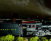 A steam engine, wheels blurred by motion, is illuminated by camera flash as it rushes by at night