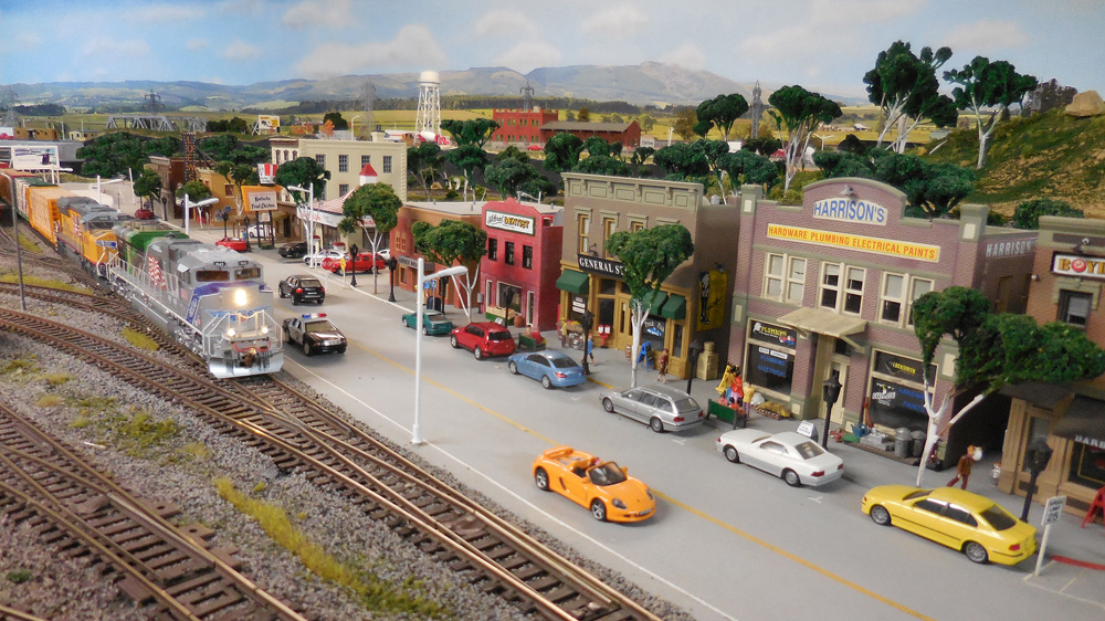 A pair of modern diesels rolls a freight train past a bustling downtown scene