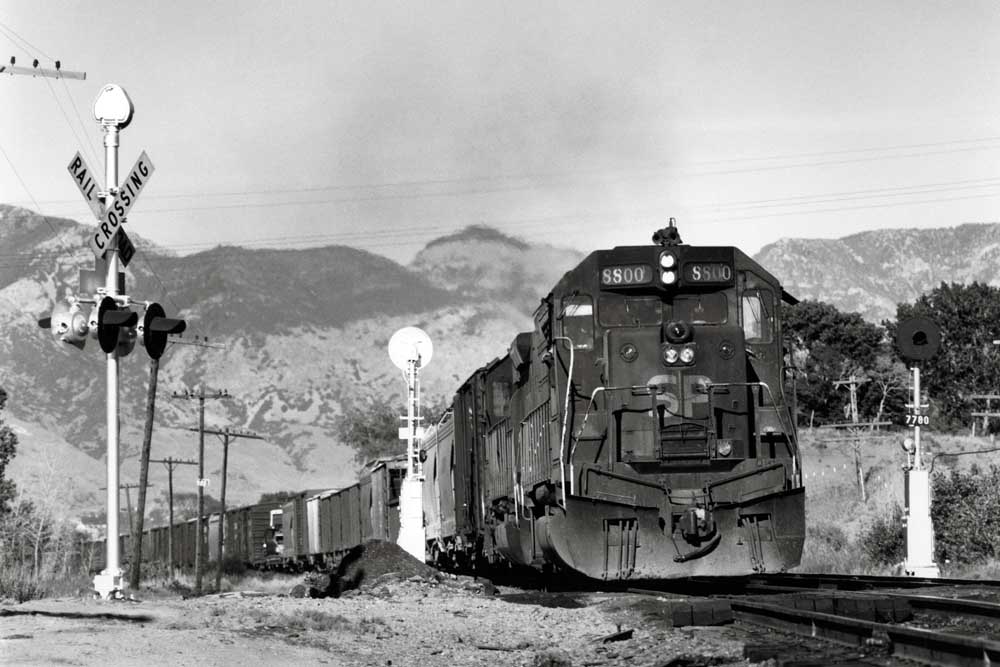 Dirty diesel locomotive leads a freight train through a road crossing