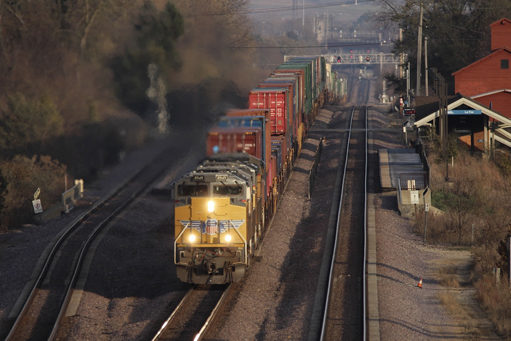 Container train with yellow locomotives approaches on the middle of three tracks.