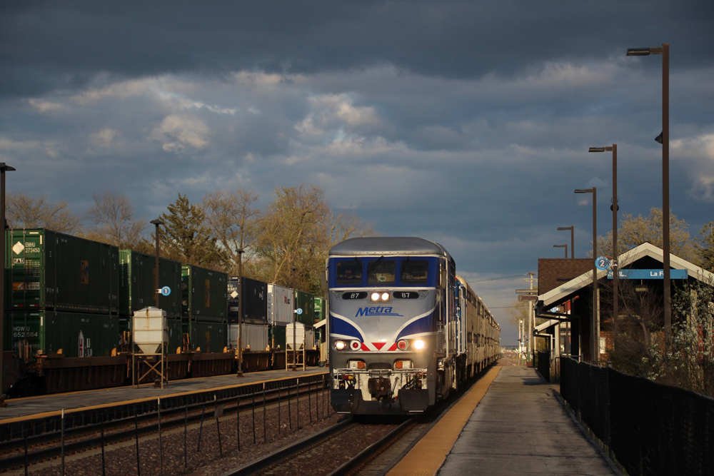 Train with blue and silver locomotive at station platform under billowing clouds.