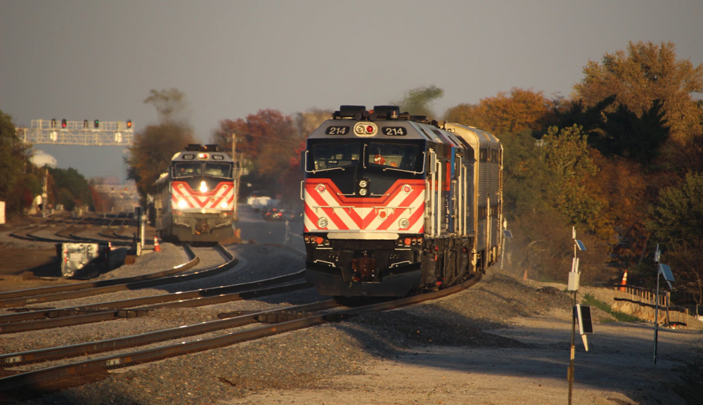 Two commuter trains with bilevel gallery cars meet in late afternoon sunlight.