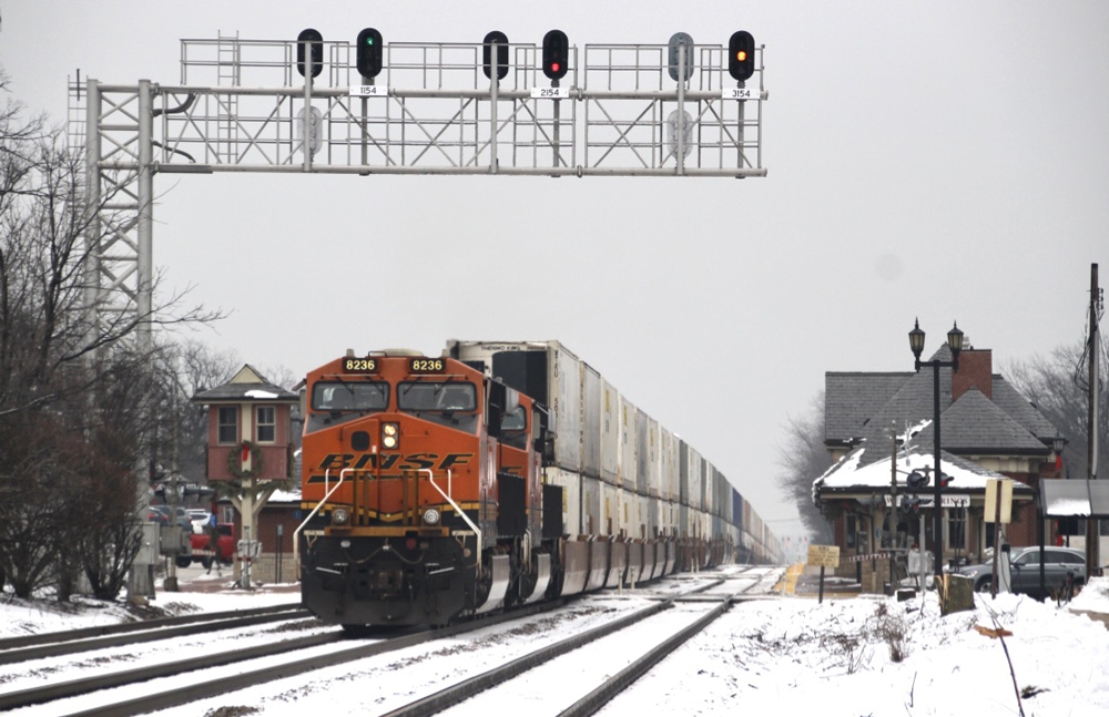 Container train rolls under signal bridge as it passes commuter station