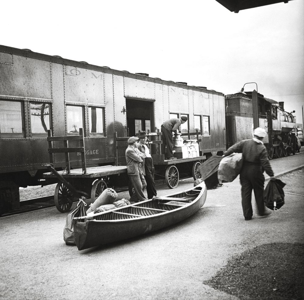 Two men stand on a train platform with a canoe