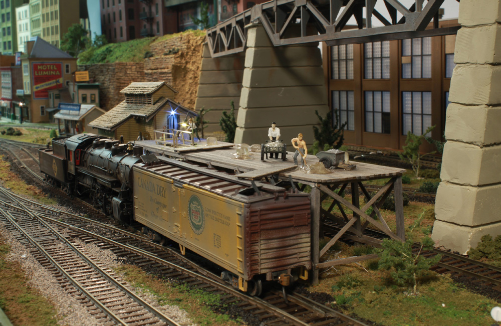 A small steam locomotive is coupled behind an ice-bunker reefer being loaded at an icing platform