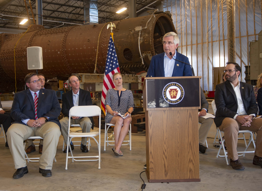 Man speaking in front of locomotive boiler in building