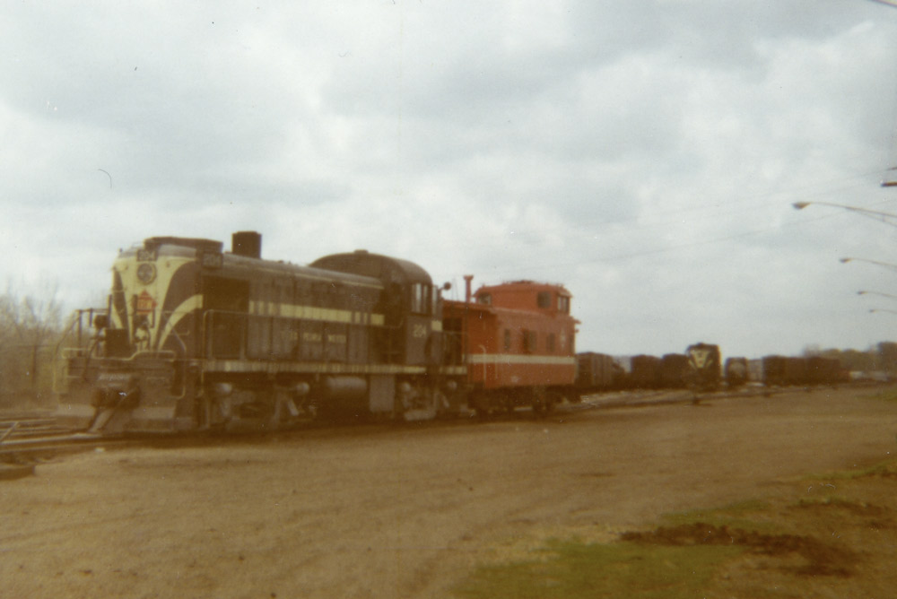 A diesel-electric locomotive and caboose at the end of a rail yard on a cloudy day.