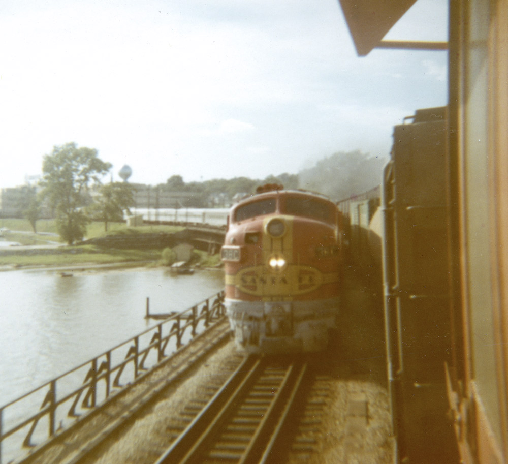 Red-and-yellow diesel-electric locomotive with double-headlight approaches the camera pulling a silver train.