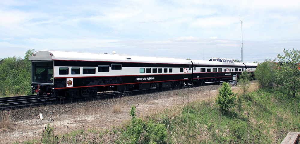 Black and white passenger cars with red trim — one with a glass back wall, one with a dome — pass on an inspection train.