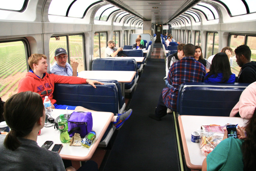 Passengers enjoying view while seated at tables in lounge car