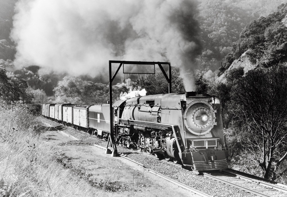 Black-and-white view of steam locomotive with freight train in mountains
