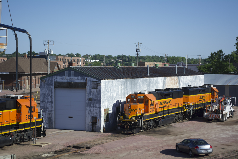 Metal enginehouse with worn white and green paint and two BNSF Ry. road locomotives parked next to it.