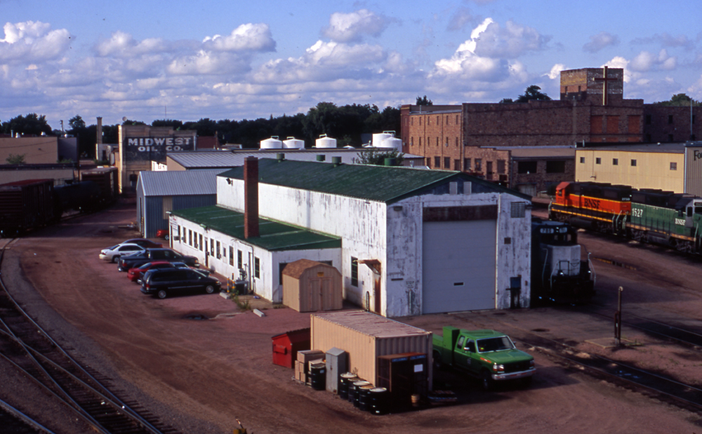 Metal enginehouse with one-story bump-out and assorted road locomotives in background.
