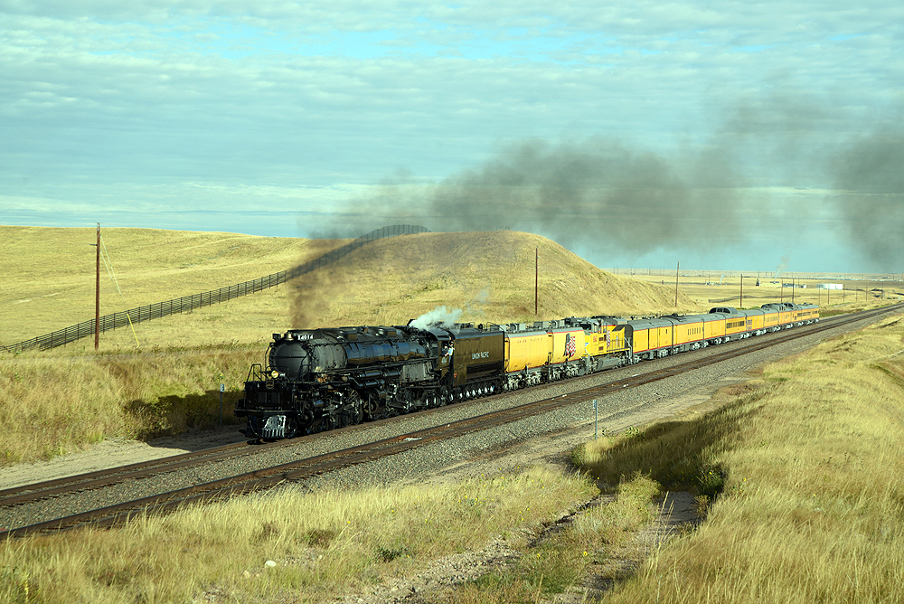 Steam locomotive with yellow passenger train in rolling hills