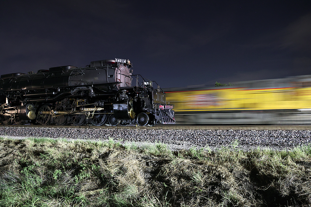 A yellow locomotive appears as a motion blur at night as the Big Boy steam locomotive is paused.