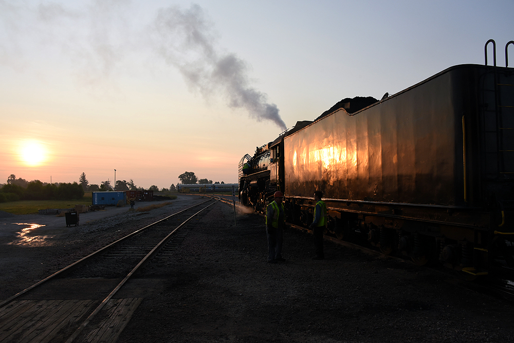 Railroad workers near a steam locomotive in low angle sunlight.