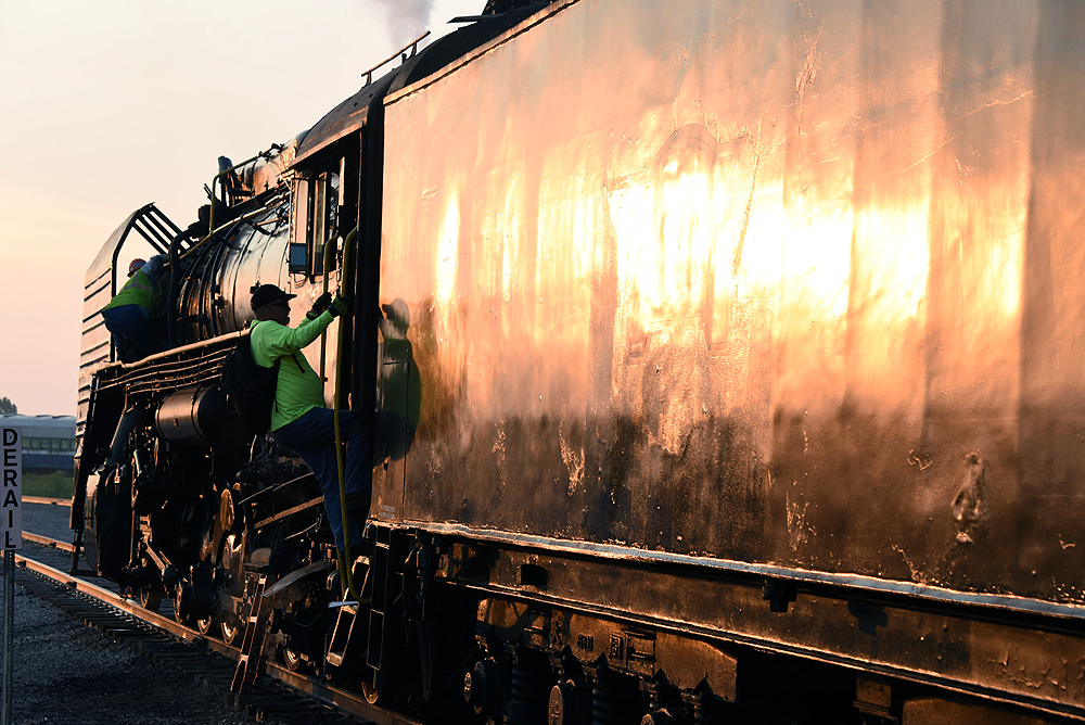 Close-up view of a steam locomotive tender reflecting low angle sunlight as a railroader climbs into a steam locomotive cab.