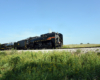 Steam locomotive hauling freight train under clear skies.