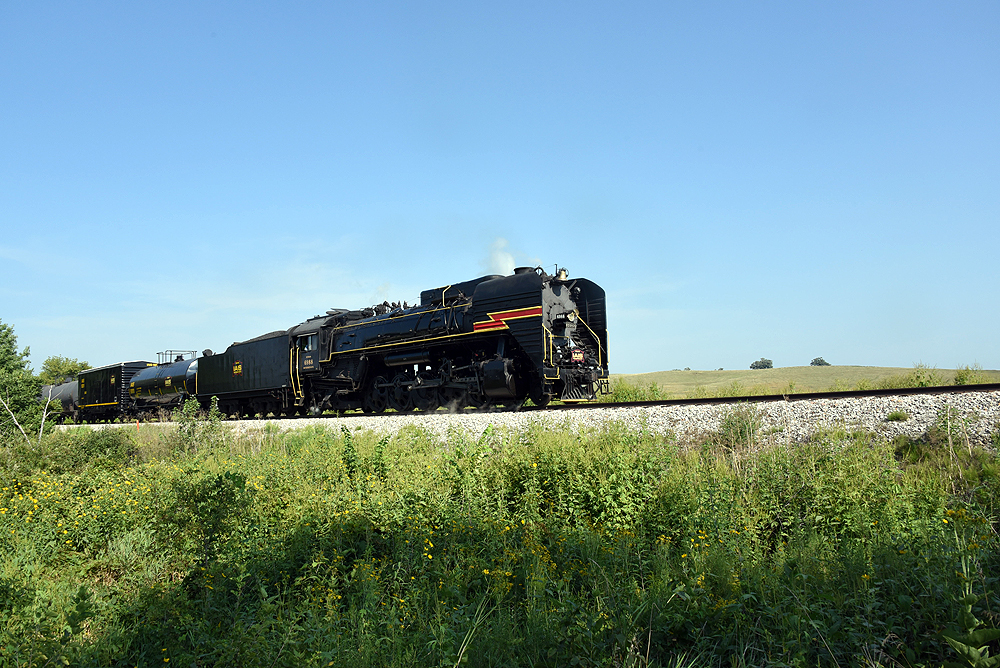 Steam locomotive hauling freight train under clear skies.