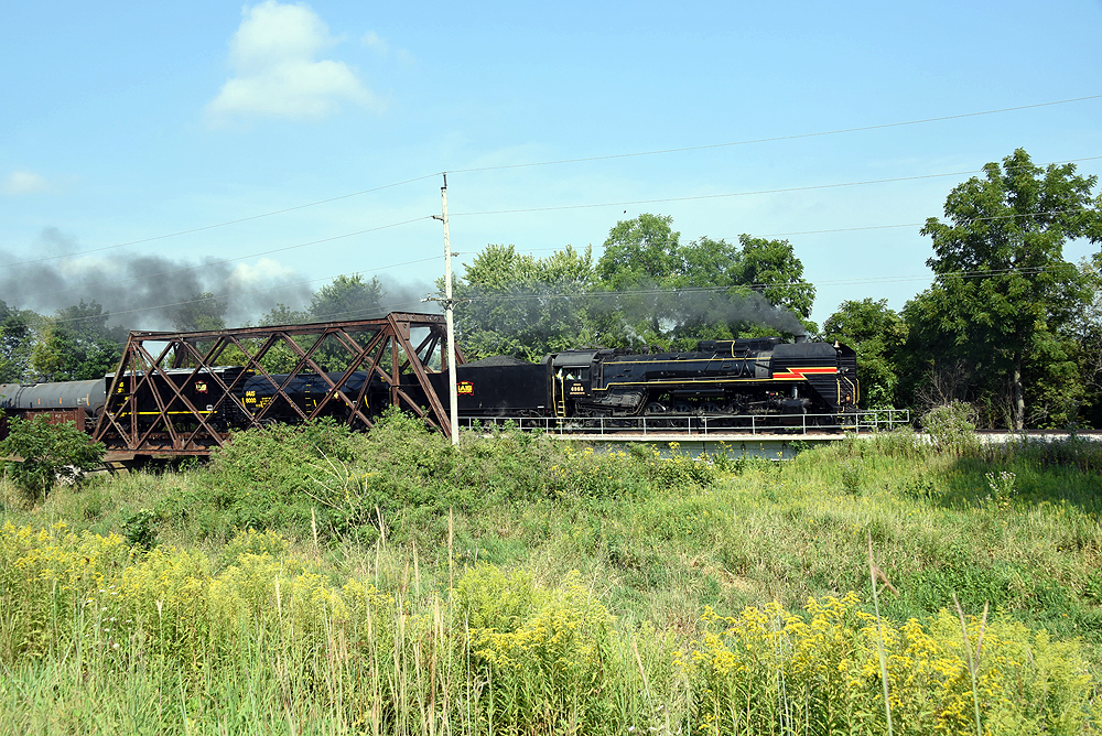 Steam locomotive hauling freight train over steel truss bridge.