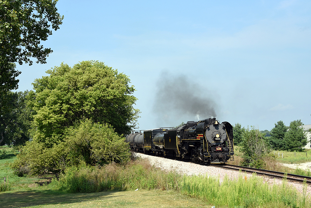 Steam locomotive hauling a freight train under clear, sunlit skies.