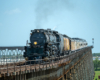 Large steam locomotive with train on long bridge seen with telephoto lens.