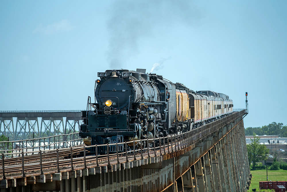 Large steam locomotive with train on long bridge seen with telephoto lens.