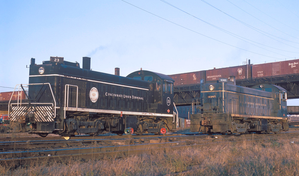 Color three-quarter-angle photo of two diesel switching locomotives on adjacent tracks.