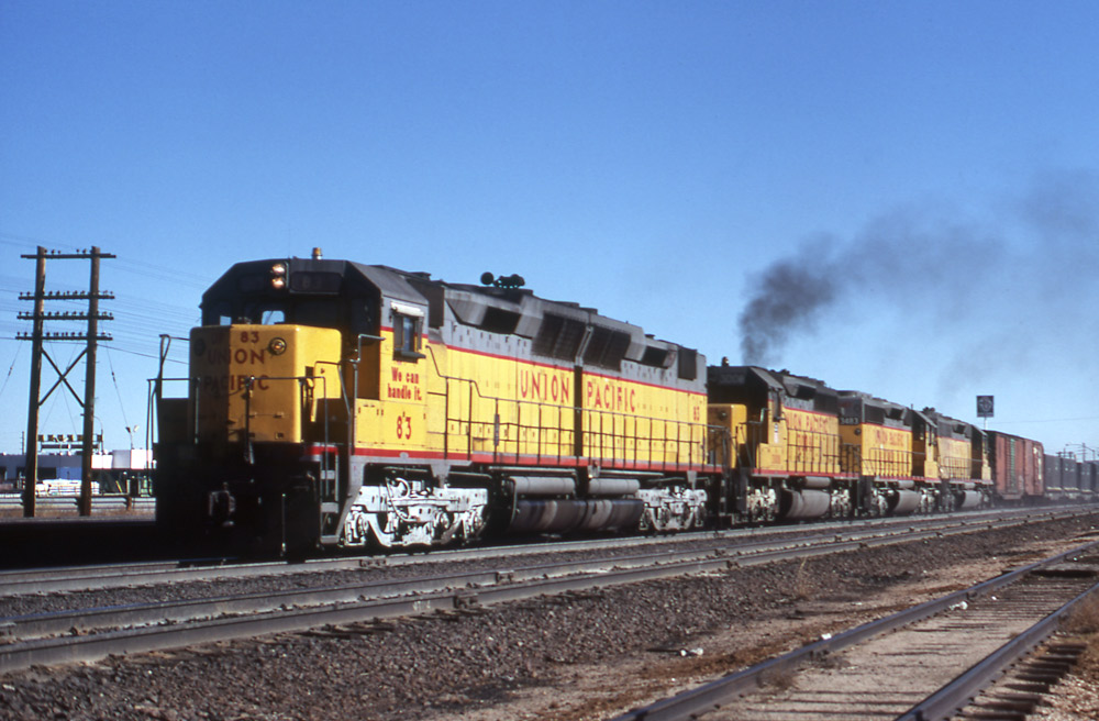 Three-quarter-angle color photo of four Union Pacific road-switcher diesel locomotives on freight train.