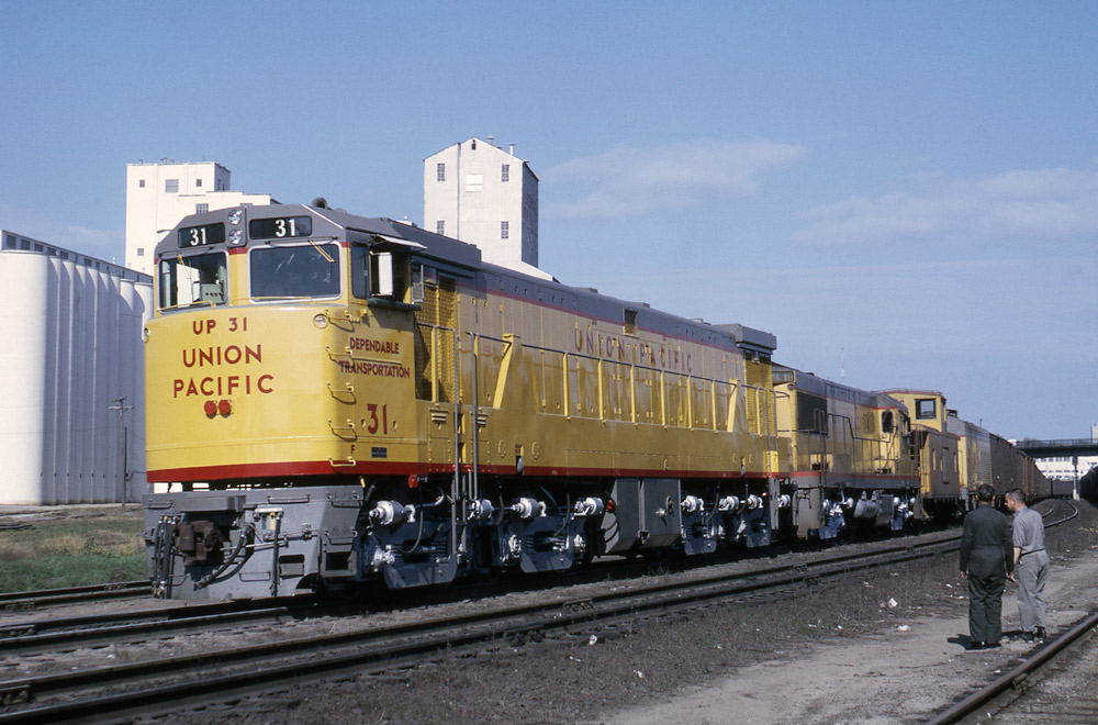 Three-quarter-angle color photo of two Union Pacific road-switcher diesel locomotives on freight train.