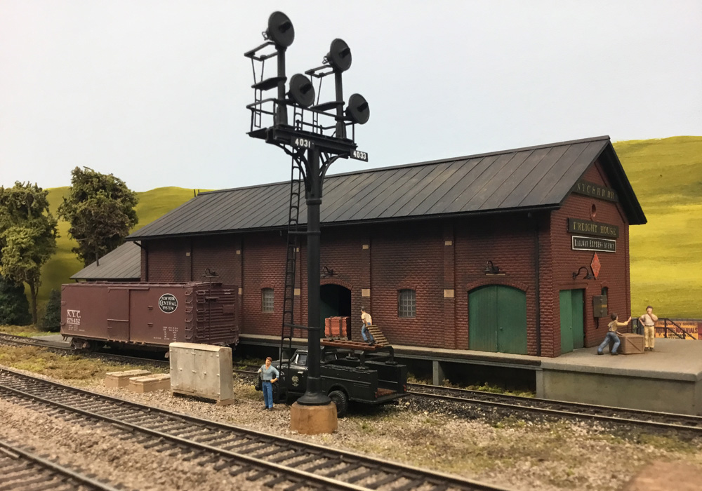 Railroad men work on the loading dock at a brick freight house where a boxcar sits