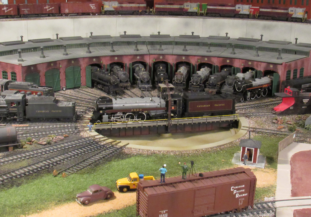 photographer standing on top of a boxcar shoots a portrait of Canadian Pacific steam locomotives lined up at a roundhouse