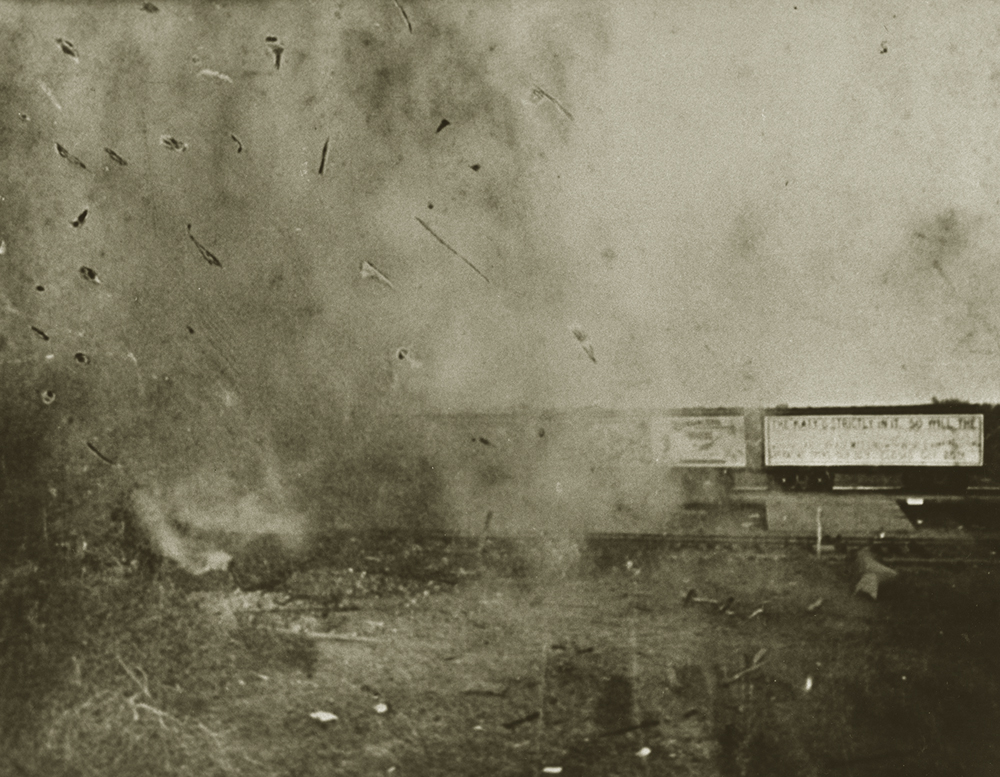 A cloud of smoke and debris with railroad cars visible to one side.