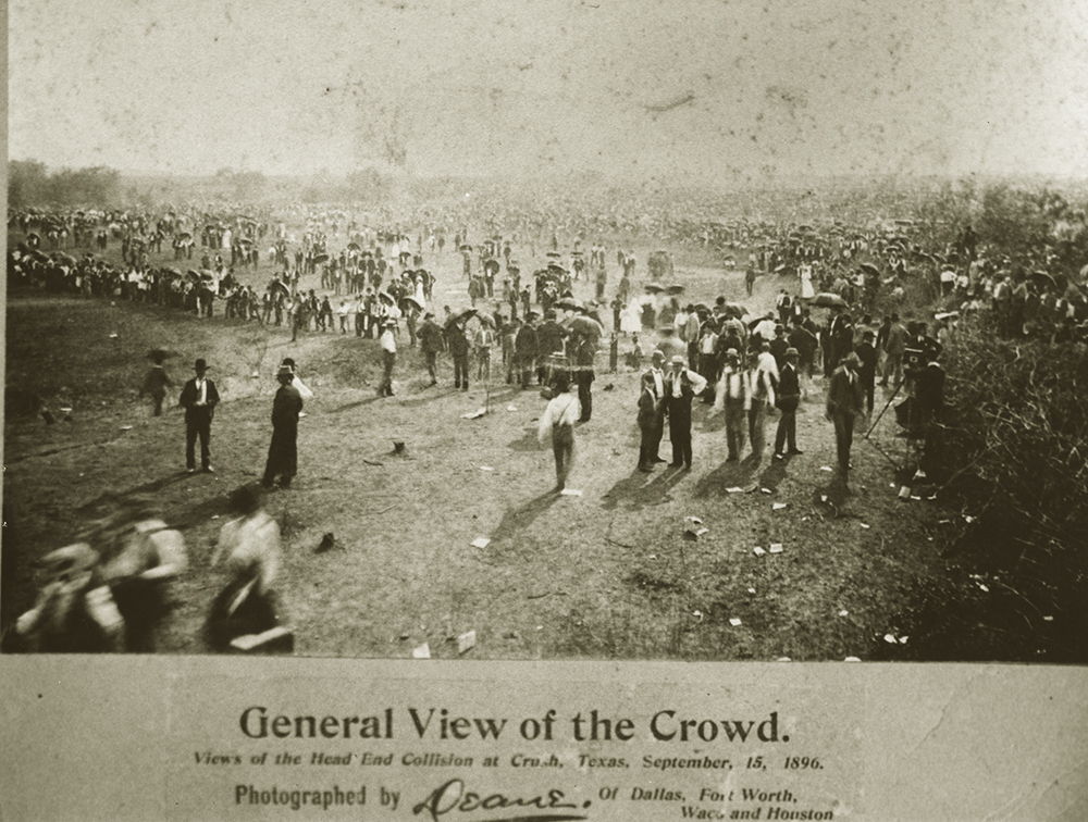 Large crowd of people, mostly men in suits and hats, in open field.