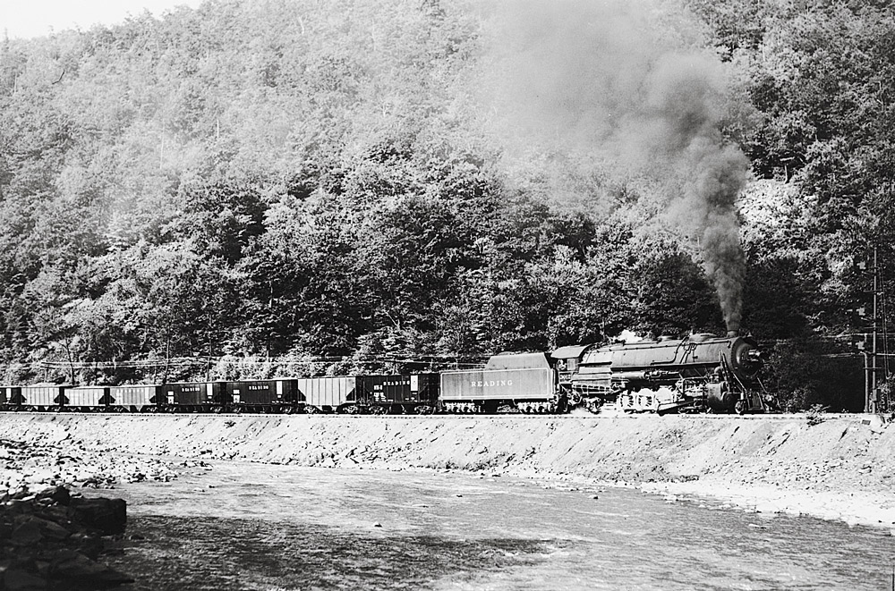 Black-and-white broadside photo of 2-10-2 steam locomotive with hopper cars beside a river