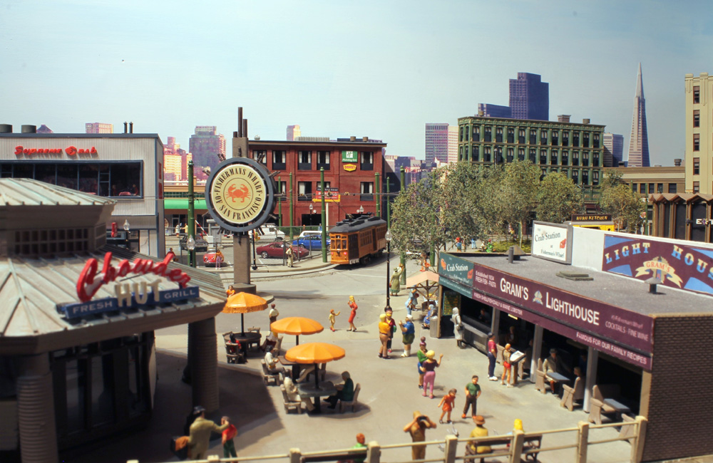 An orange trolley passes the iconic Fisherman’s Wharf sign while tourists stroll the San Francisco tourist attraction