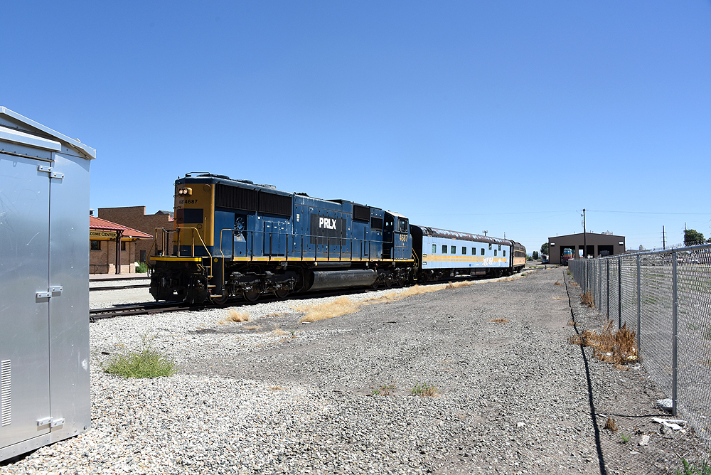 Blue and yellow locomotive shoves passenger cars on a rail siding.