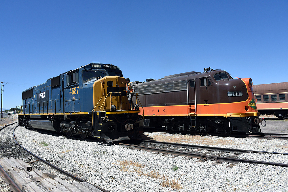 A homely looking blue-and-yellow locomotive stands to the left of a chocolate-brown and orange cab locomotive.