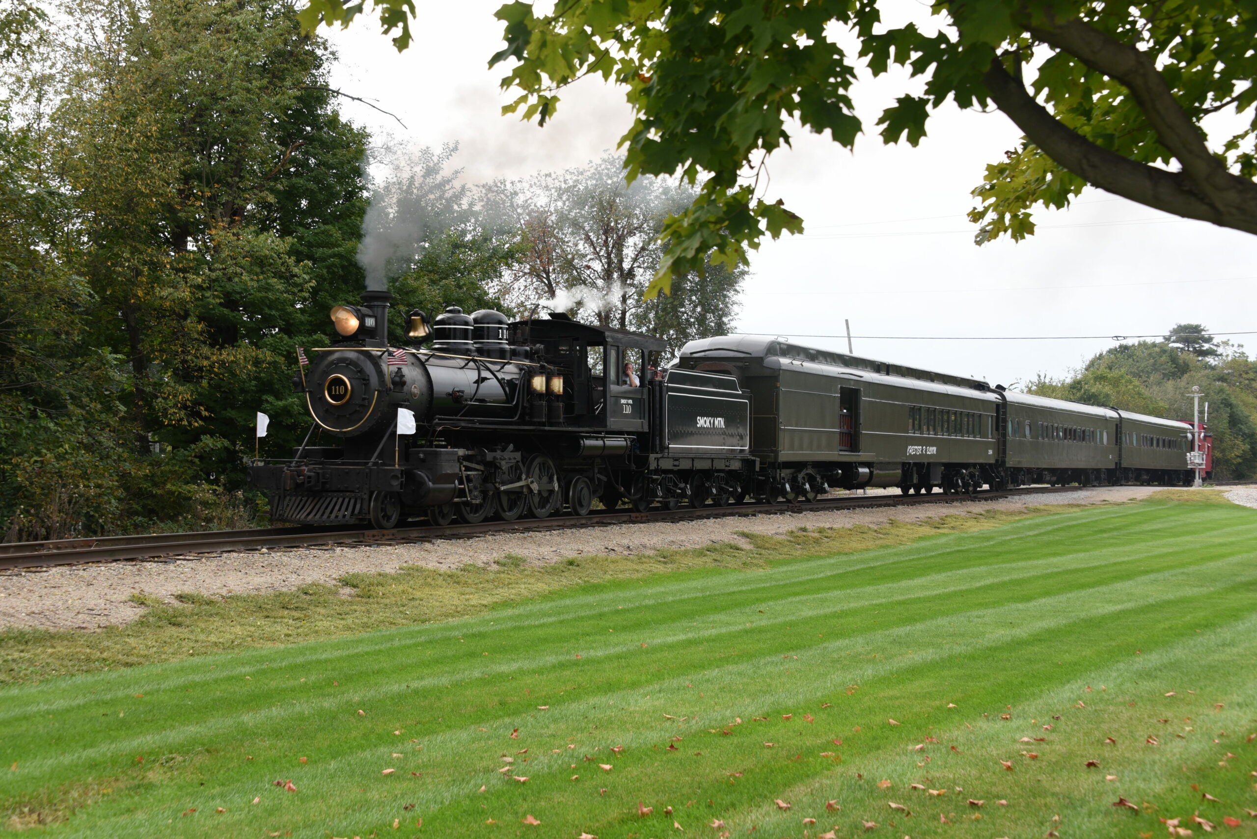 The engineer in cab of the world's smallest pacific locomotive takes the small black steam locomotive and its train for excursion.